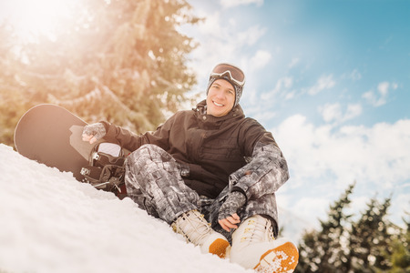 Beautiful young smiling man with snowboard enjoying a sunny winter day. Looking at camera.の写真素材