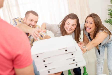 Four cheerful friends enjoying pizza together at home party. Selective focus.の写真素材