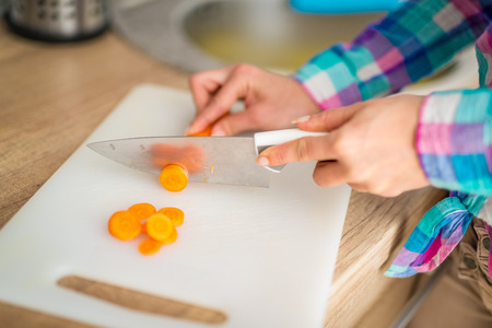 Close-up of a female hands cutting carrot on the kitchen board.の写真素材