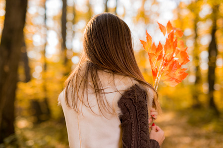 Rear view of a beautiful pensive woman with leaf in sunny forest in autumn colors.の写真素材