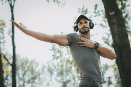 Young sportsman with headphones doing stretching exercise in the park.