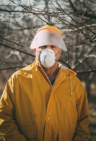 Portrait of a mature man with mask spraying tree with chemicals in the orchard before winter. Looking at camera.の写真素材