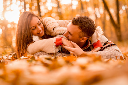 Beautiful smiling couple enjoying in sunny forest in autumn colors. They are lying on the falls...