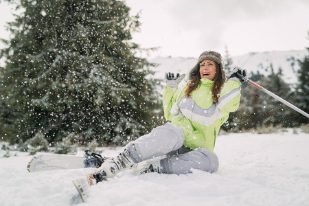 Beautiful young female skier falling down on mountain slope.