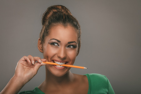Beautiful young smiling woman biting pencil and thinking.の写真素材