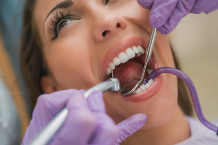 Beautiful young woman in visit at the dentist office. She is sitting on a chair and dentist repair teeth on her. Selective focus. Close-up.の写真素材
