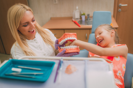 Beautiful little girl at visit in the dentist office. She and female dentist having fun with big...