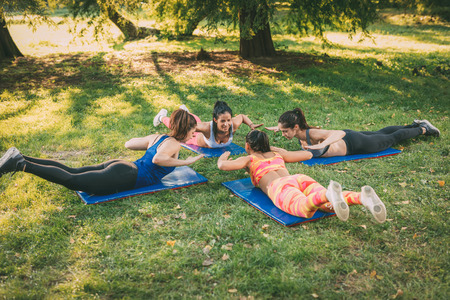Four beautiful female friends doing plank exercise in the park. の写真素材