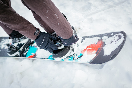 Close-up of man hands adjusting bindings on snowboard boot.の写真素材