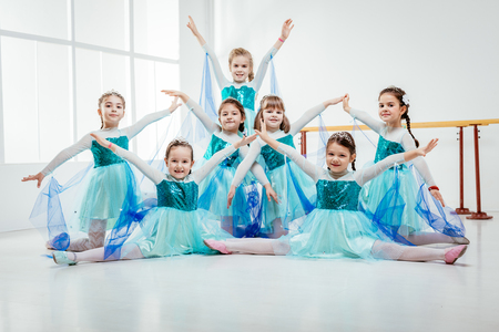 Smiling little girls in dresses practicing postures during ballet class. Looking at camera.の写真素材