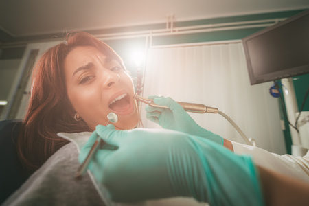 Beautiful young woman in visit at the dentist office. She is sitting on a chair and dentist repair teeth on her. Selective focus.の写真素材