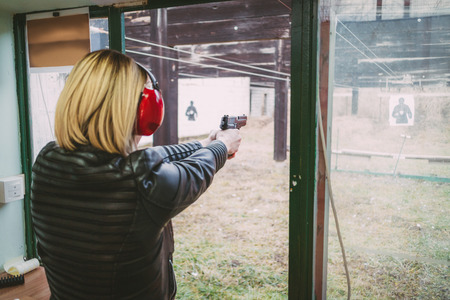 Woman firing with pistol on target at the shooting range. Rear view.の写真素材