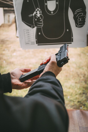 Close-up of a man hands holding and loading gun magazine in the pistol at the shooting range.の写真素材