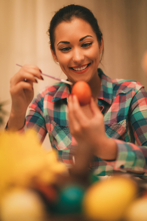 Beautiful smiling young woman painting Easter egg at home.の写真素材