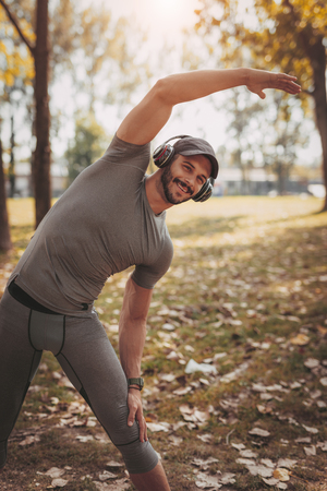 Young smiling sportsman with headphones doing stretching exercise in nature.の写真素材