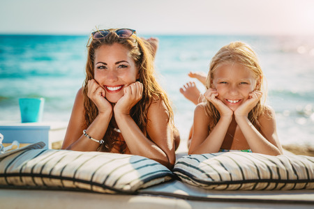 Cute little girl with her beautiful mother enjoying on the beach. Looking at camera.