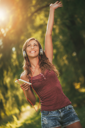 Happy beautiful girl enjoying music in the park.の写真素材
