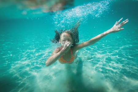 Beautiful little girl diving underwater in the sea. She is holding her nose with hand and holding breat.の写真素材