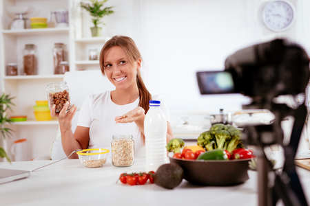 Beautiful young woman filming her blog broadcast about healthy food at the home.の写真素材