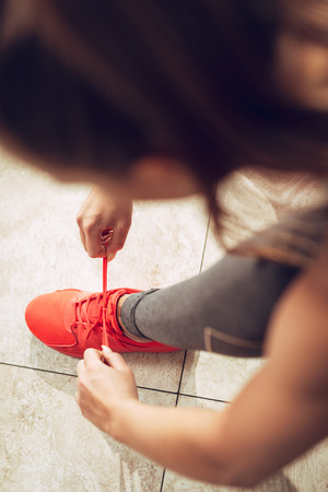Beautiful girl getting ready for workout at the gym. She is tying shoelace on sneakers. Top view.の写真素材