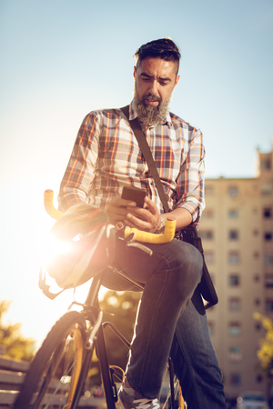 Casual businessman going to work by bicycle. He is sitting on a bike and sending text message.の写真素材