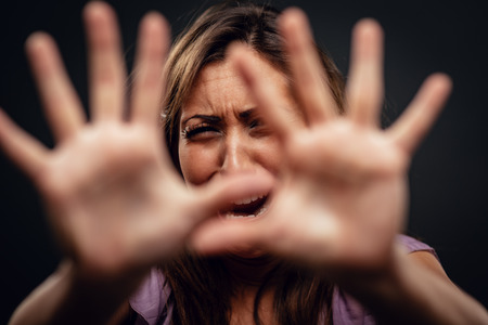Young abused woman defending with pray looking at camera with outstretched arm. Selective focus. Focus on background, on woman face.の写真素材