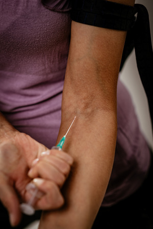 Close-up of a female drug addiction with a belt around her arm injecting drugs with syringe.の写真素材