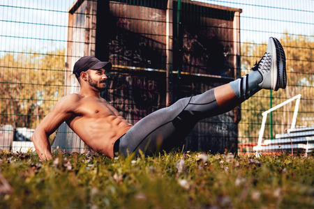 Young urban muscular sportsman doing sit-ups exercise in the park.