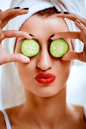 Beautiful young woman having fun and covering eyes with sliced cucumber for facial mask.の写真素材