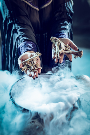 Close-up of a witch's hands holding bones above boiling water for a cooking poison soup.の写真素材