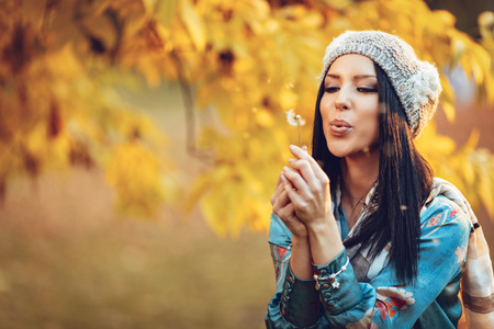 Portrait of young positive beautiful smiling young woman blowing dandelion in autumn park.の写真素材
