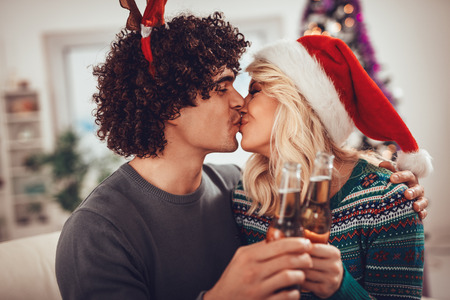 Young romantic couple hugging and kissing in Christmas time. They are toasting with bottles of drink.の写真素材