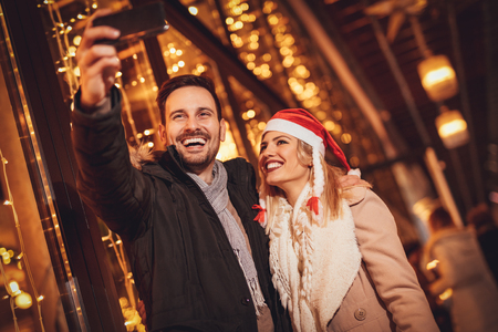 Two beautiful cheerful young people taking selfie in the shopping mall with bright shop window in background.   
の写真素材