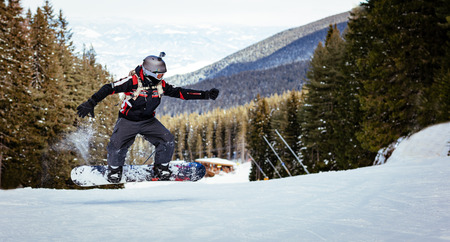 Snowboarder jumps on mountain slopes and enjoying a sunny winter day.