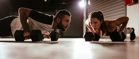 Young muscular couple doing push-up exercise with dumbell on hard workout at the garage.の写真素材