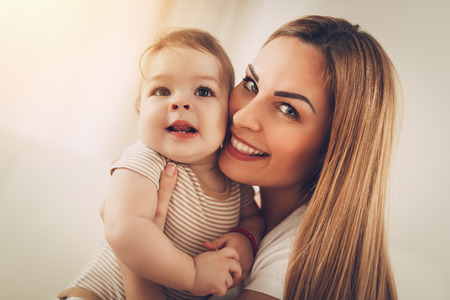 Beautiful young mom having fun with her cute baby boy at the home. Looking at camera