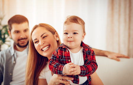 Beautiful baby boy enjoying at the home with his parents. They are sitting on sofa and playing.の写真素材