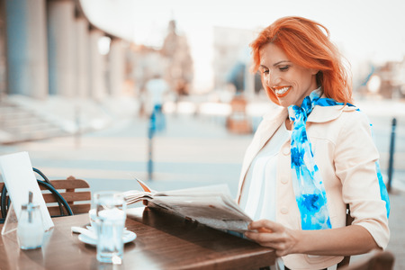 Smiling businesswoman On A Break reading newspaper in a street cafe.の写真素材