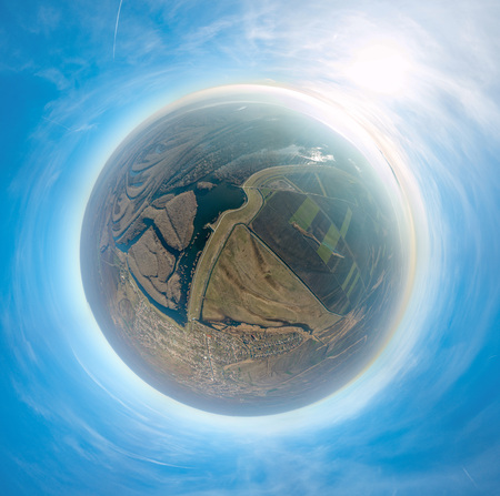 Panorama of the river's valley with fields and village in a form of a little planet on a blue sky background.の写真素材