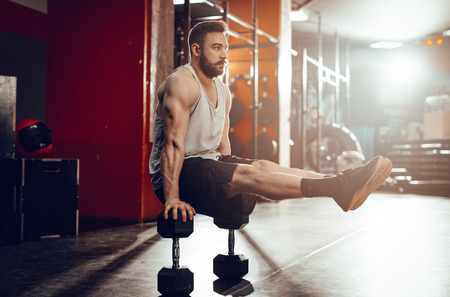 Young muscular man doing hard exercise at the gym. His whole weight is on dumbbells.