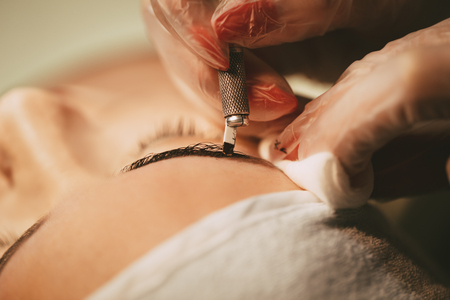 Close-up of a beautician hands applying permanent eyebrow makeup to model.  の写真素材