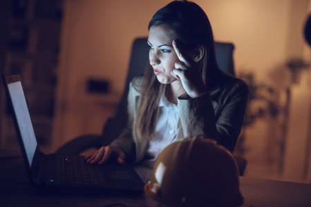 Worried lonely young woman looking at lighted screen of a laptop in night at the home. She is tired because working late.の写真素材