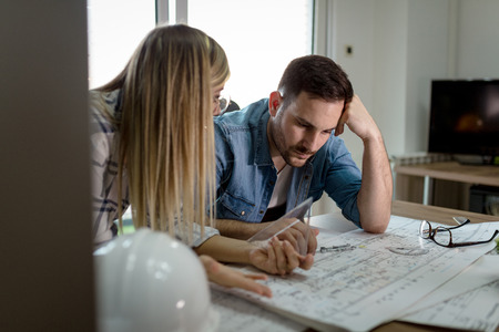 Young worried architect colleagues talking and analyzing blueprints while working on a new project at the office.の写真素材