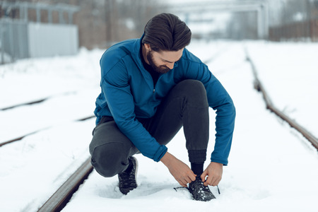 Urban jogger tying running shoes and making pause during stretching and exercises in the winter training outside in.の写真素材