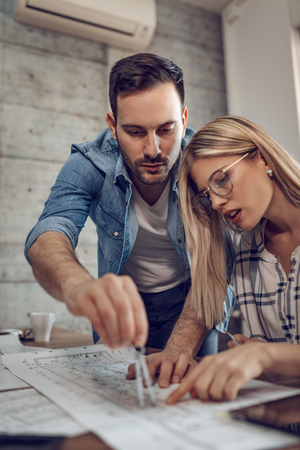 Young architect colleagues talking and analyzing blueprints while working on a new project at the office.の写真素材