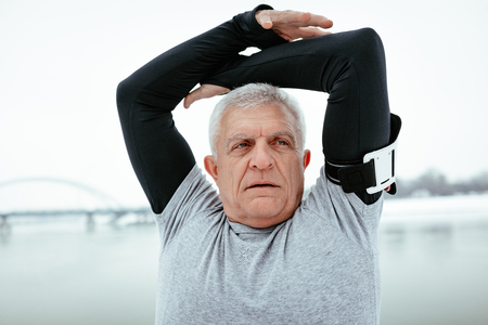 Close up of active senior man stretching and doing exercises by the river during the winter training outside in.の写真素材