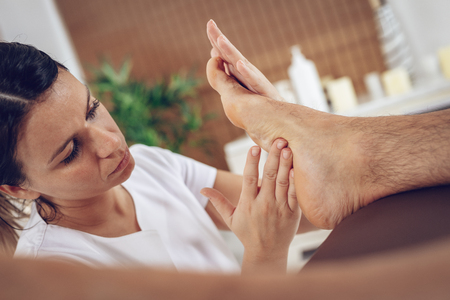 Close-up of a young female therapist massaging young man's foot at beauty salon.の写真素材