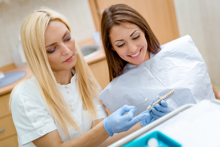Beautiful young smiling woman at visit in the dentist office and female dentist showing her porcelain crowns. の写真素材
