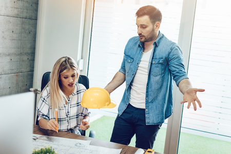 Young worried architect colleagues talking and analyzing blueprints while working on a new project at the office.の写真素材