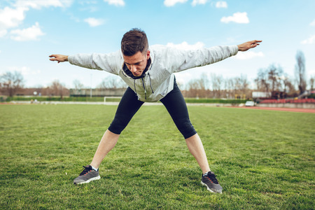 Active young man stretching and doing exercises in the public place on empty stadium. の写真素材